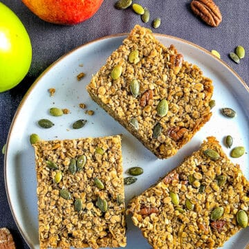 three maple syrup flapjack bars on a plate topped with pumpkin seeds.