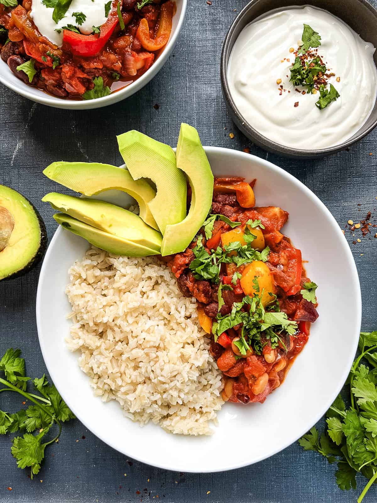 bean chilli served in a bowl with brown rice and sliced avocado with a side of soured cream.
