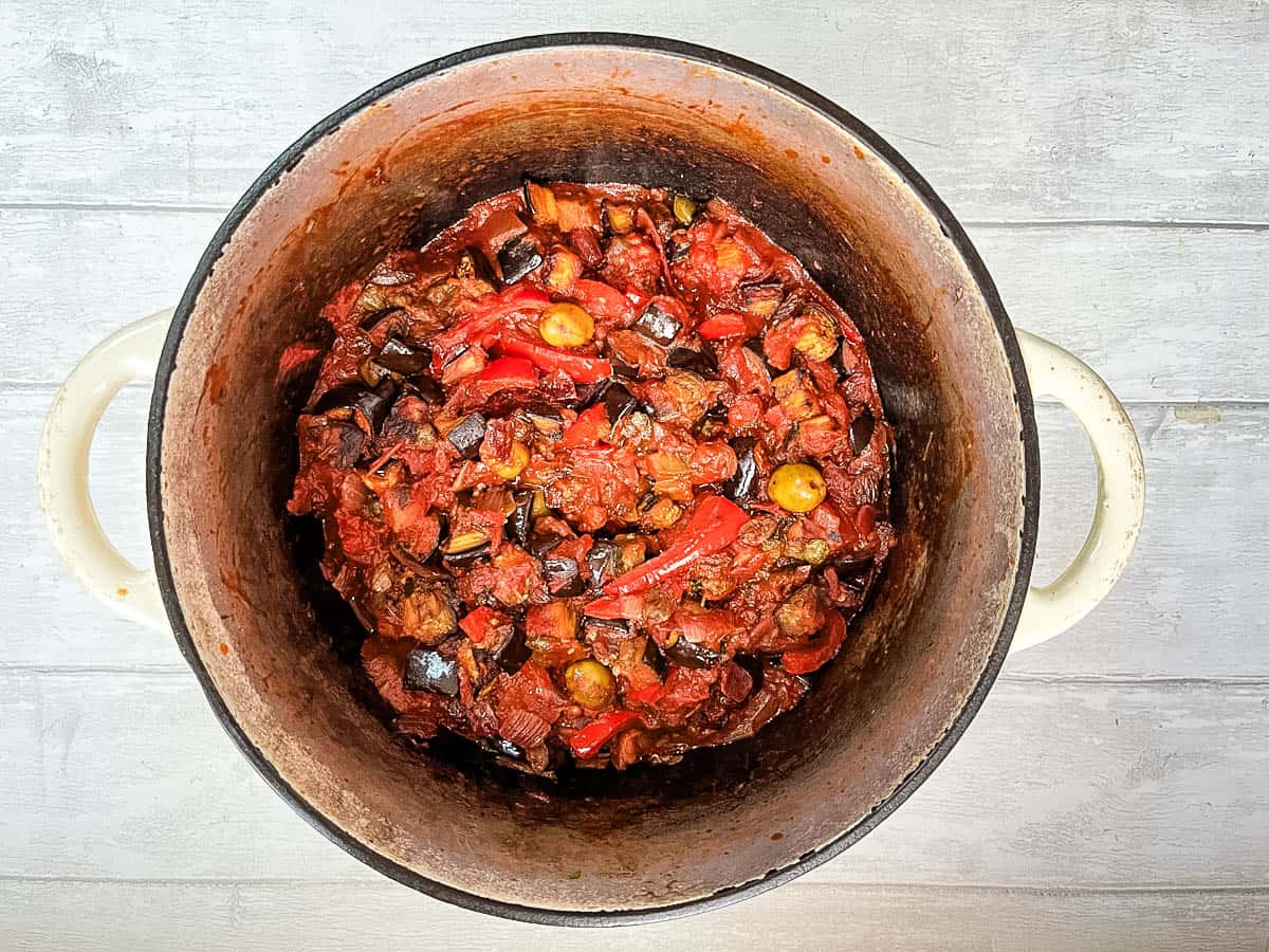 aubergine green olives capers and tomatoes simmering in pan.