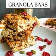 stack of granola flapjacks on plate with pumpkin seeds and dried cranberries.