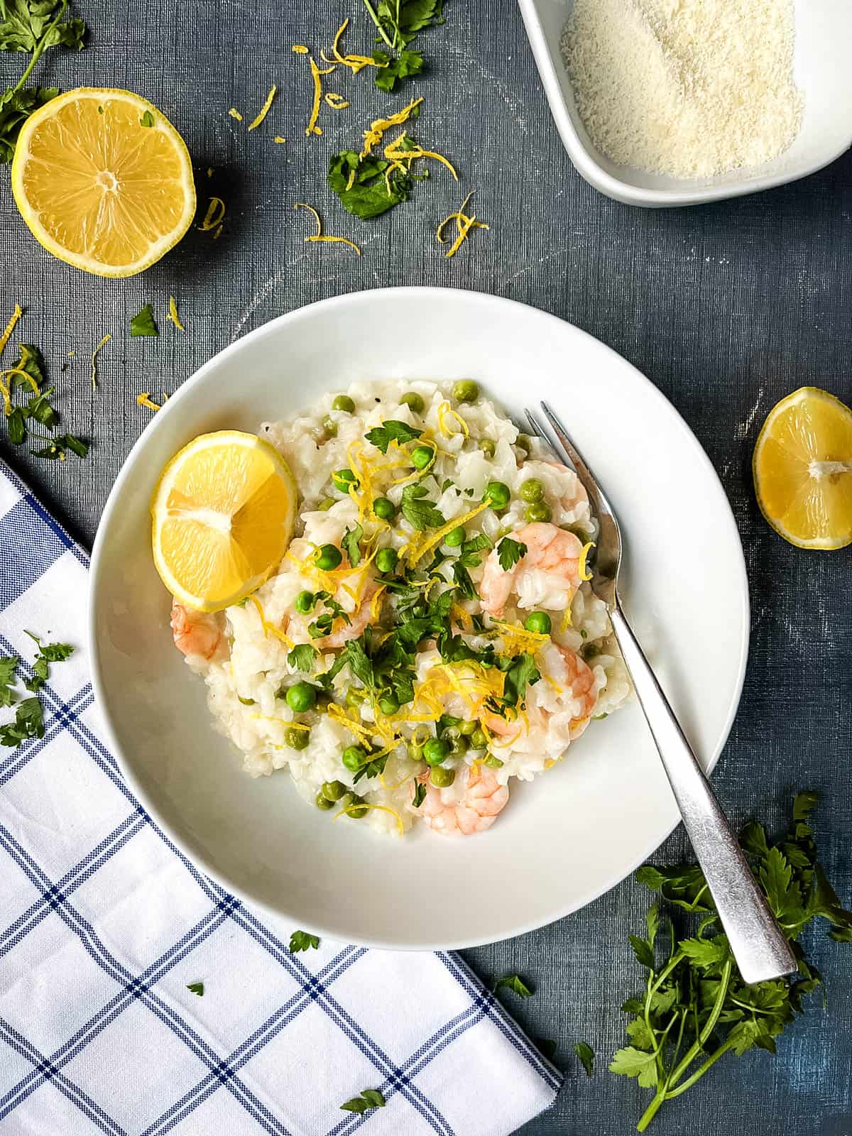 prawn and pea risotto served with lemon and topped with fresh parsley and lemon zest in a bowl.