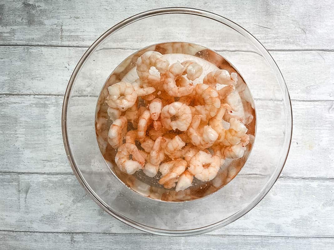 cooked prawns defrosting in bowl of cold water.