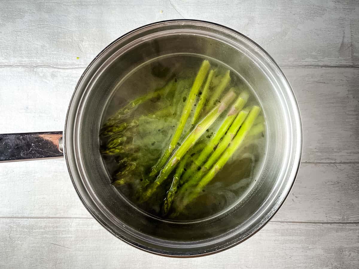 asparagus simmering in stock in pan.