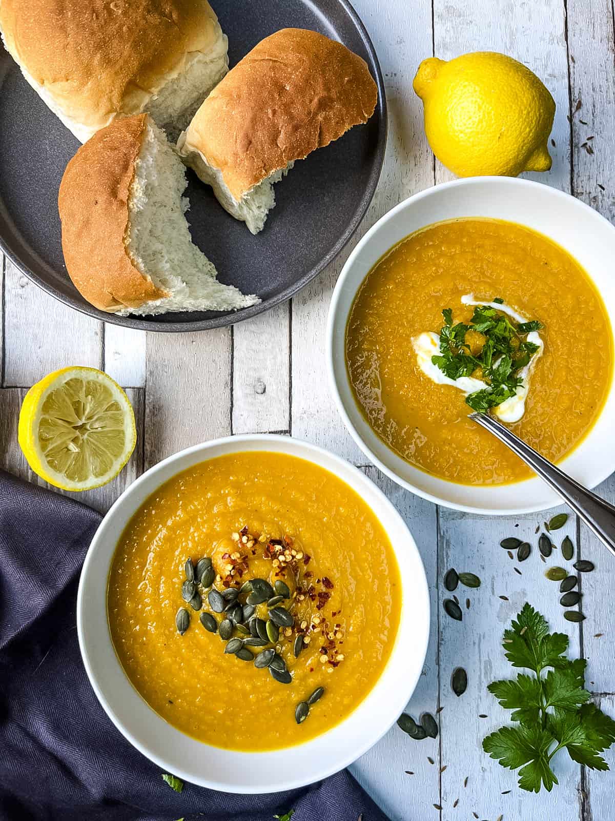 carrot and cumin soup in bowls served with bread rolls.