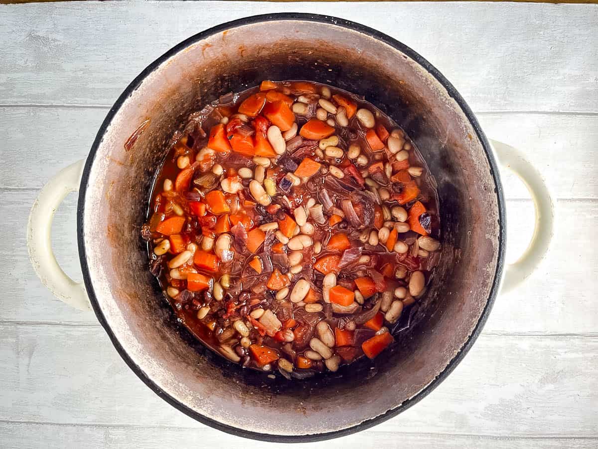 mixed beans added to chopped tomatoes onion and carrot in casserole dish.