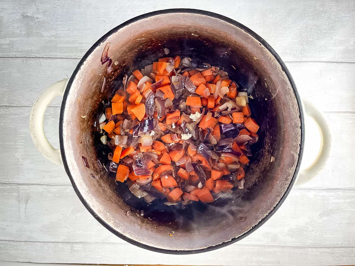 red onions and diced carrots frying in stove top pan.