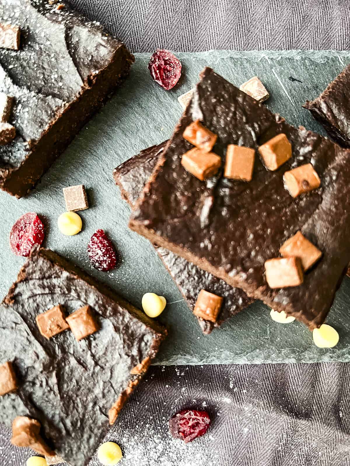 chocolate brownies topped with chocolate chips and cranberries on a slate.