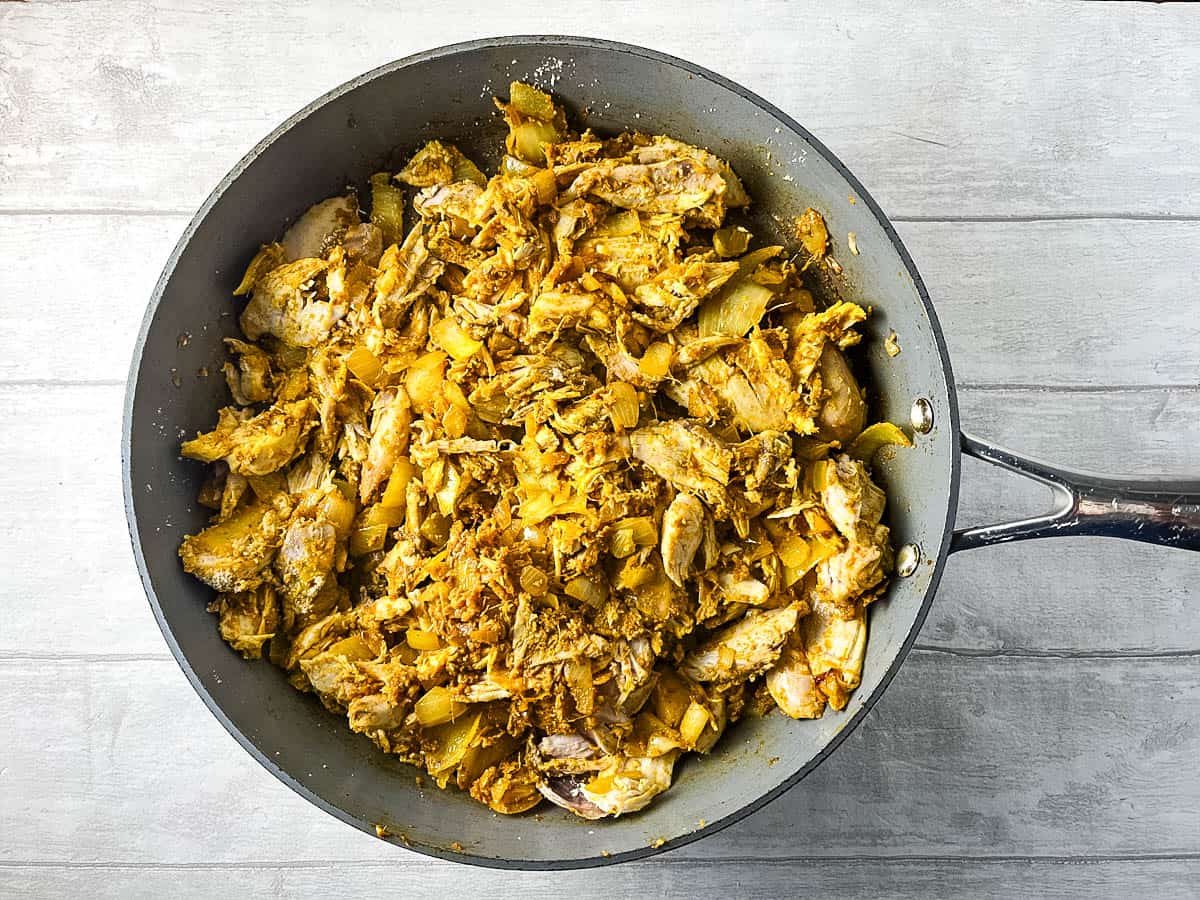 cooked chicken mixed with curry paste in a frying pan.