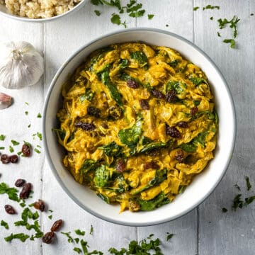 chicken curry in bowl on a board with sultanas, coriander and garlic to side.