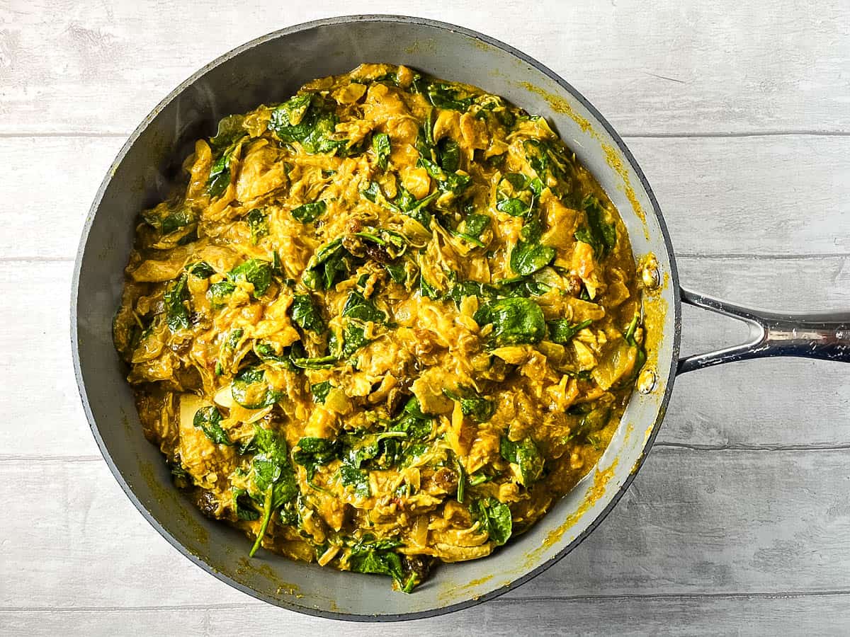 fresh spinach leaves added to chicken curry in pan.