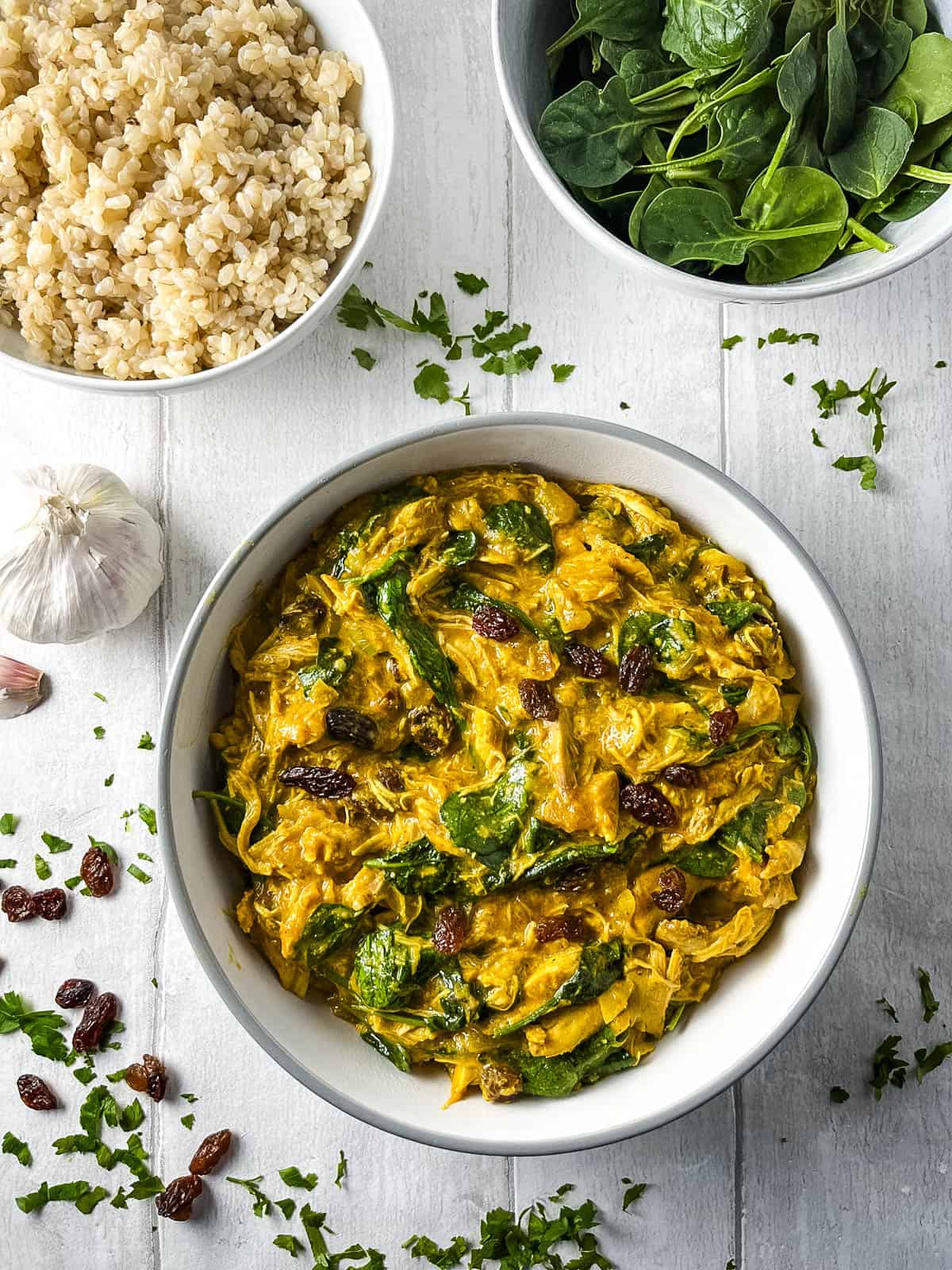 chicken curry in a bowl with bowl of spinach leaves and rice to side.