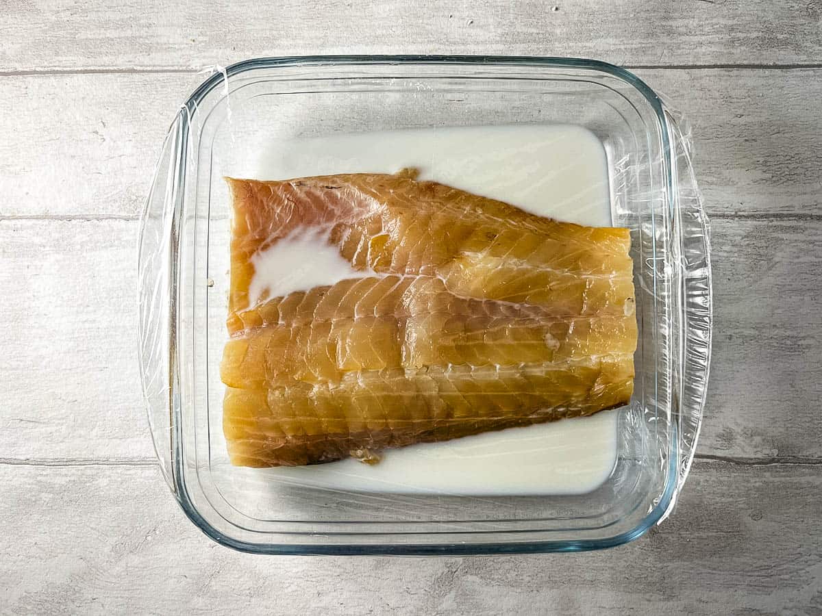 smoked haddock fillet in a glass dish with milk and covered with clingfilm ready for poaching in microwave.