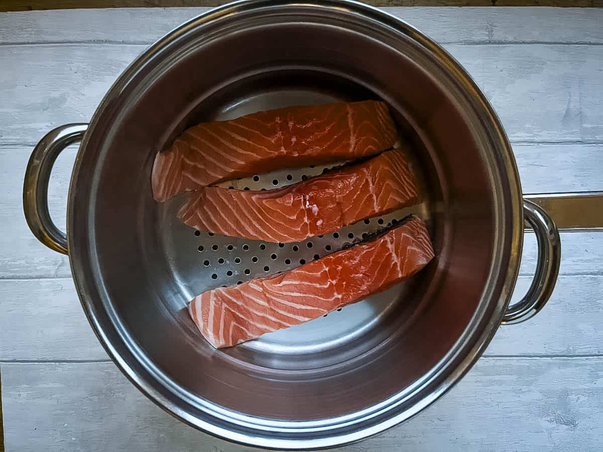 salmon fillets in a colander steaming over a pan.