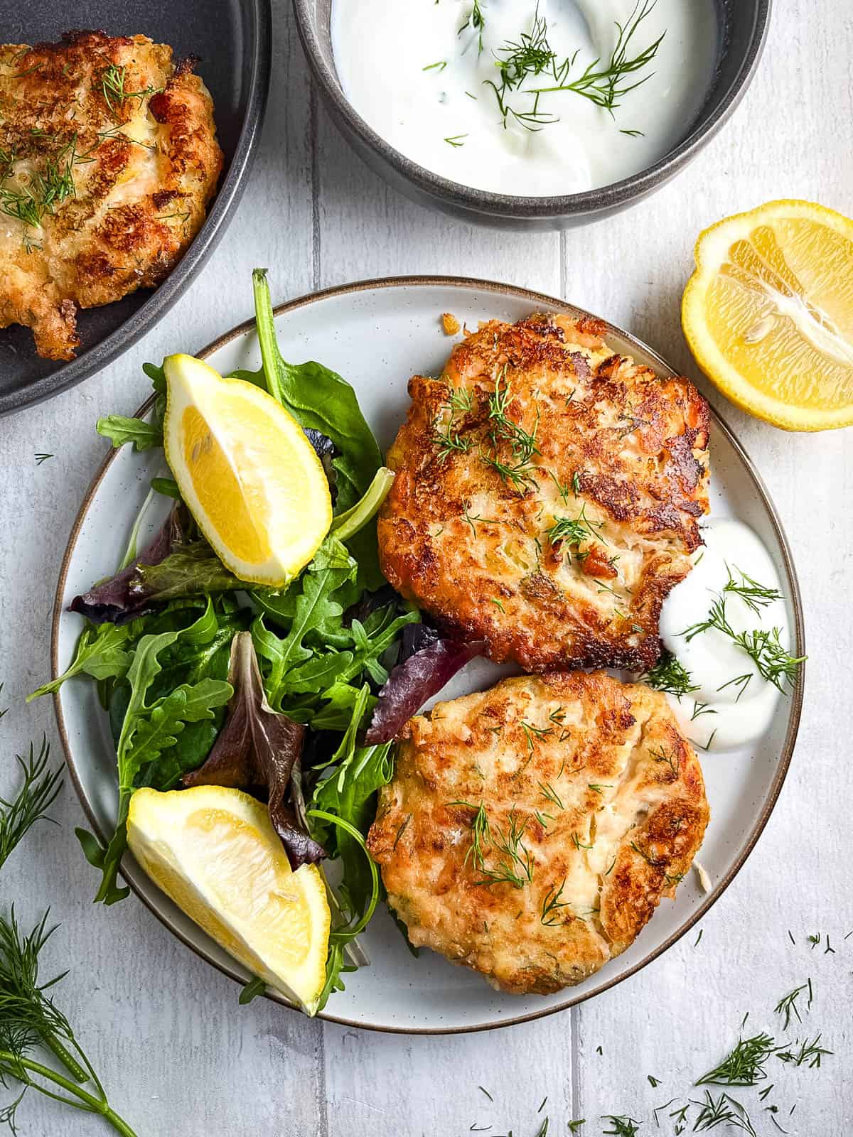 two salmon fishcakes on a plate with a green salad and lemon wedges.