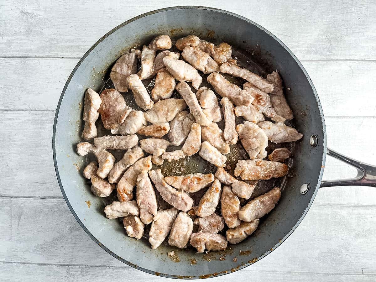 pork tenderloin strips frying in pan.