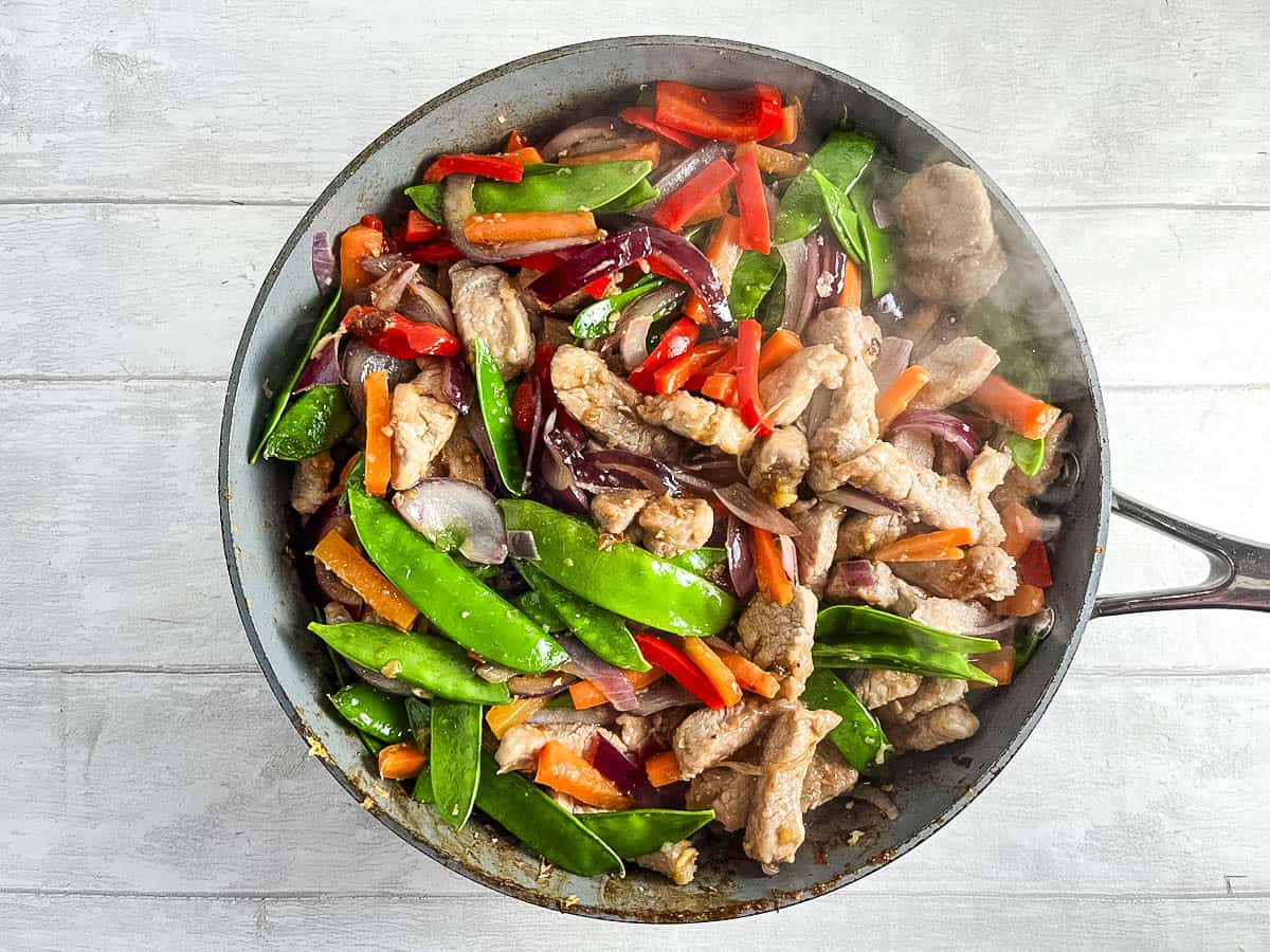 pork strips in pan with red pepper, mange tout, red onion, garlic and honey.