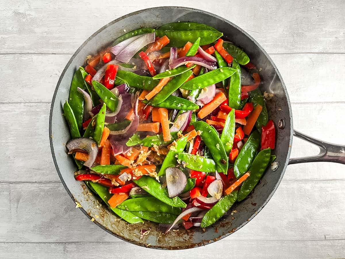 red onion, red pepper, mangetout, garlic and ginger frying in pan.