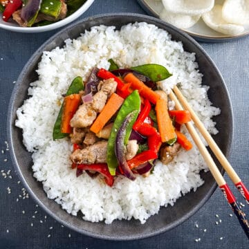 pork stir fry in a bowl with rice and chop sticks.