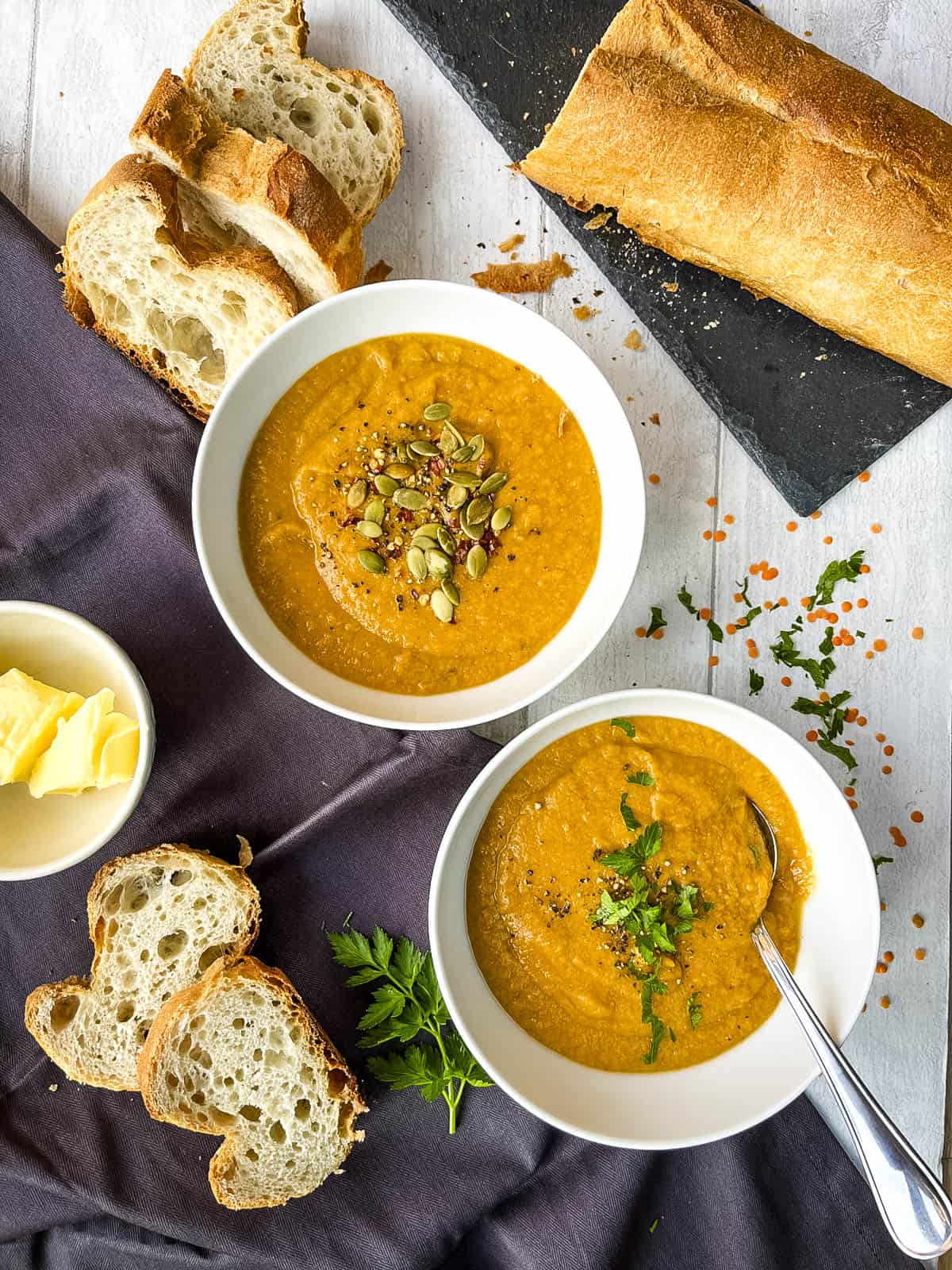 two bowls of leek and red lentil soup topped with parsley and pumpkin seeds served with bread