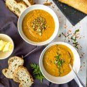 two bowls of leek and red lentil soup topped with parsley and pumpkin seeds served with bread