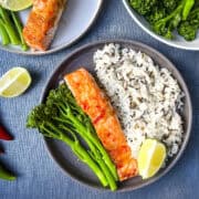 baked salmon fillet on plate with wild rice, tender stem broccoli and wedge of lime.