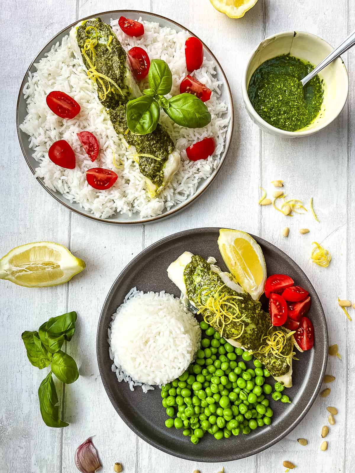 two plates of tray baked cod and pesto served with rice and tomatoes.