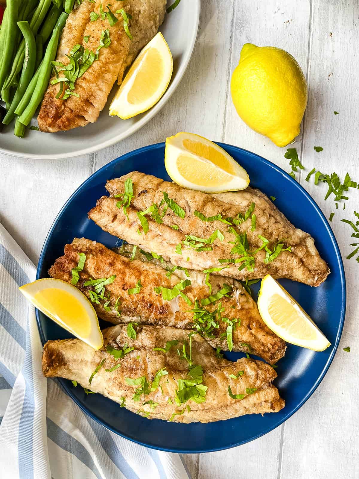 plate of sea bream fillets pan fried and served with fresh parsley and lemon wedges.