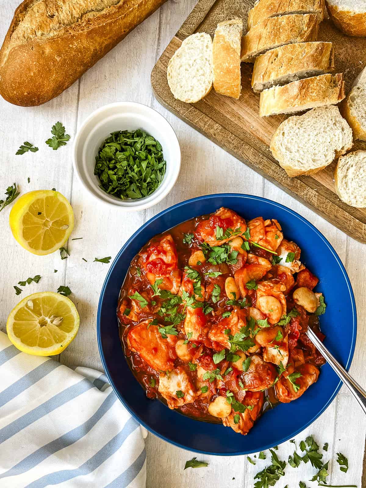 white fish stew in bowl topped with fresh parsley with crusty bread to side.