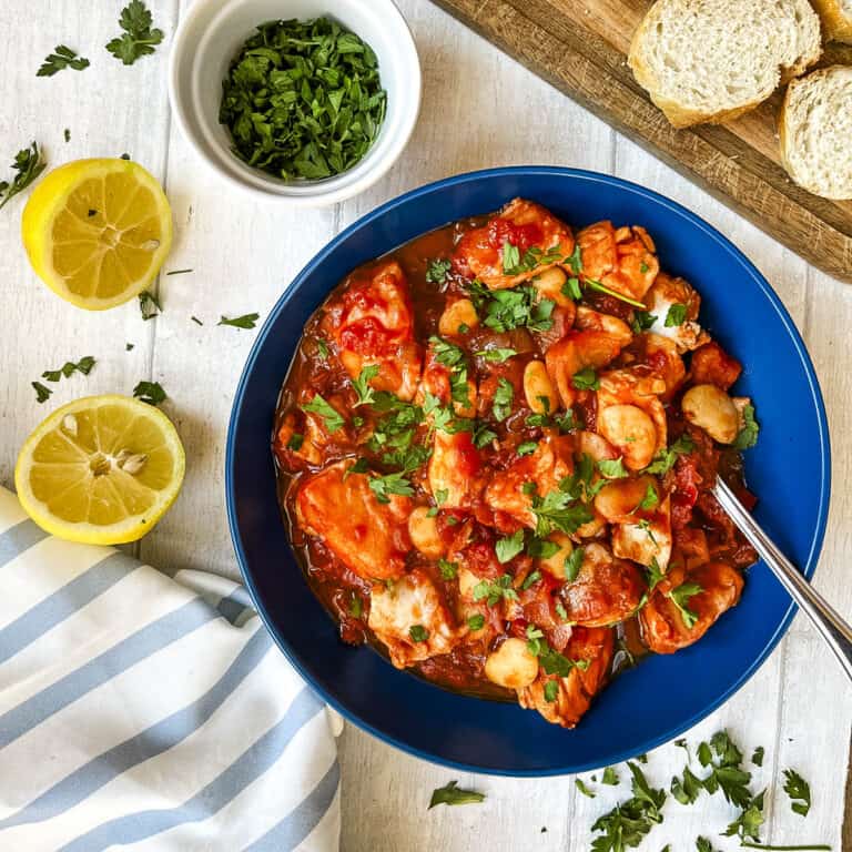 bowl of white fish stew served with crusty bread and topped with fresh parsley.
