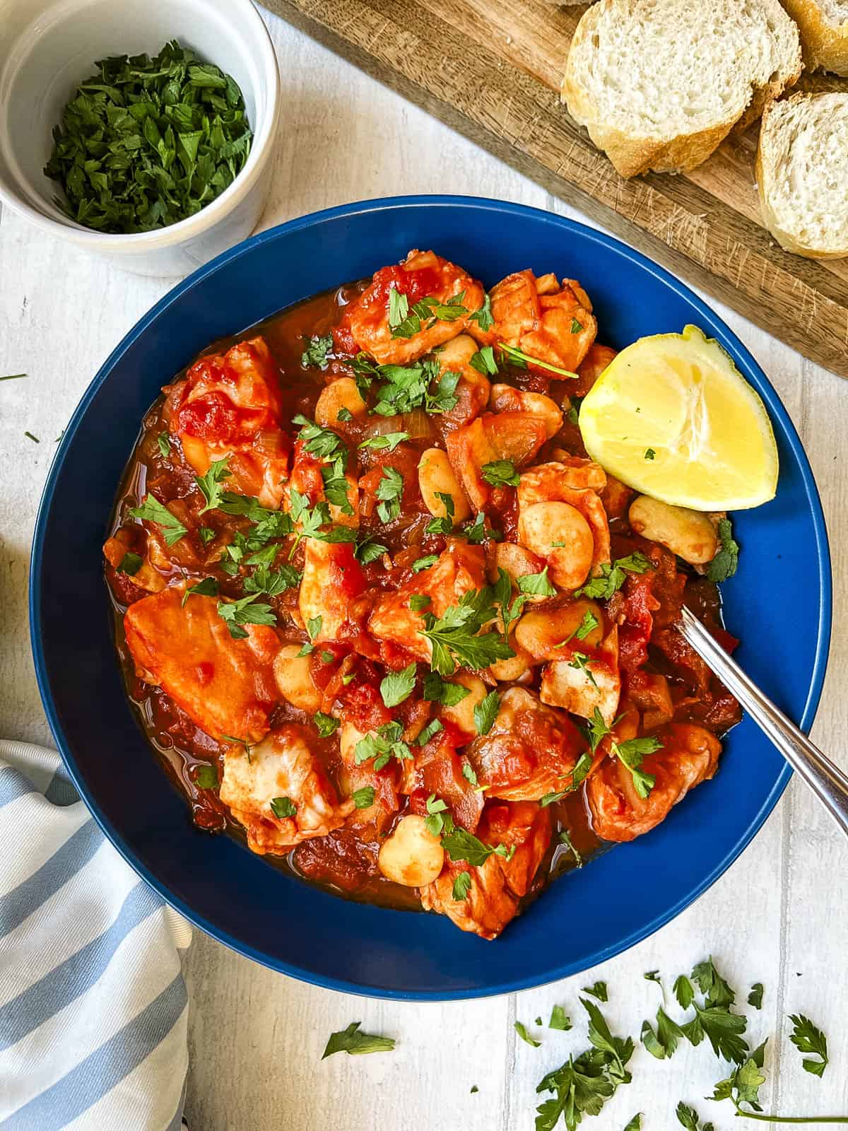 bowl of white fish stew served with a wedge of lemon and topped with fresh parsley.