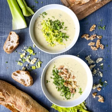 two bowls of stilton and celery soup topped with celery leaves and walnuts.