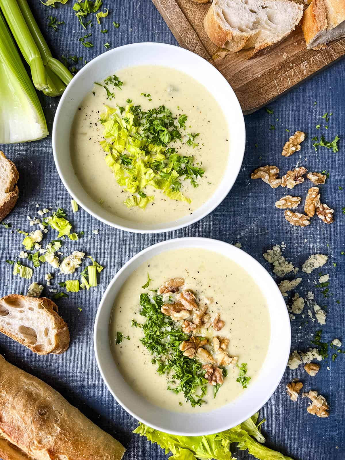 two bowls of stilton and celery soup topped with walnuts celery leaves and parsley.