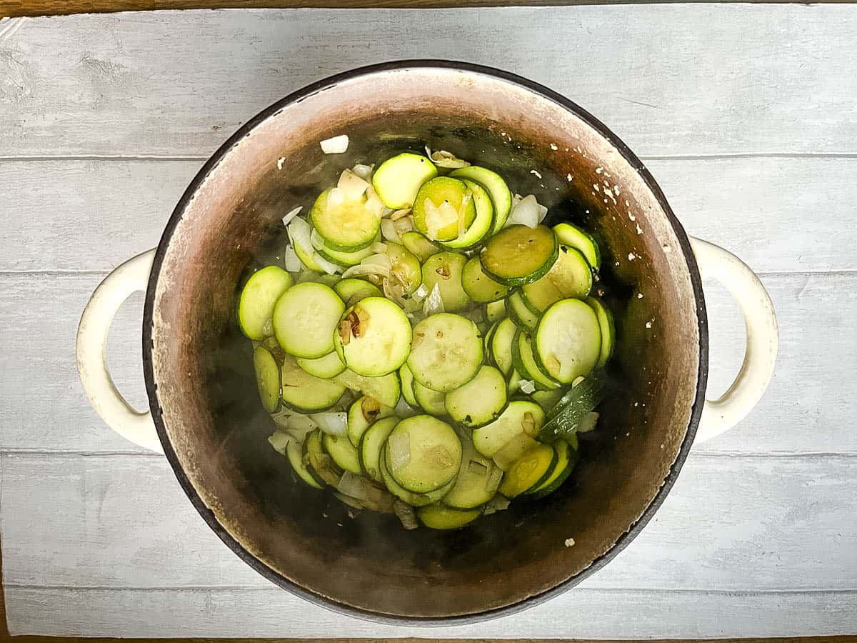 fried onion, garlic and sliced courgette in a stove top casserole dish.