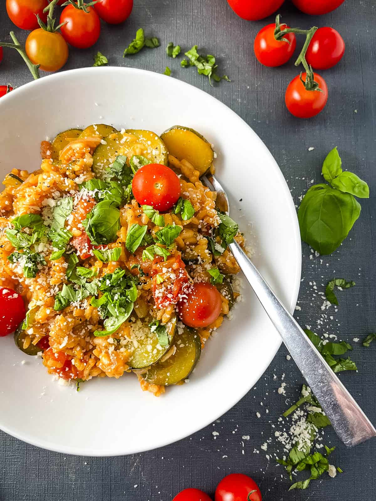 bowl of tomato and courgette risotto topped with fresh basil leaves.