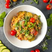 bowl of tomato and courgette risotto topped with basil leaves and parmesan cheese
