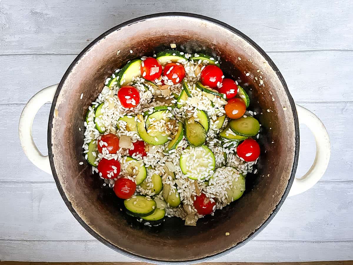 risotto rice added to courgettes, cherry tomatoes and onion in pan.