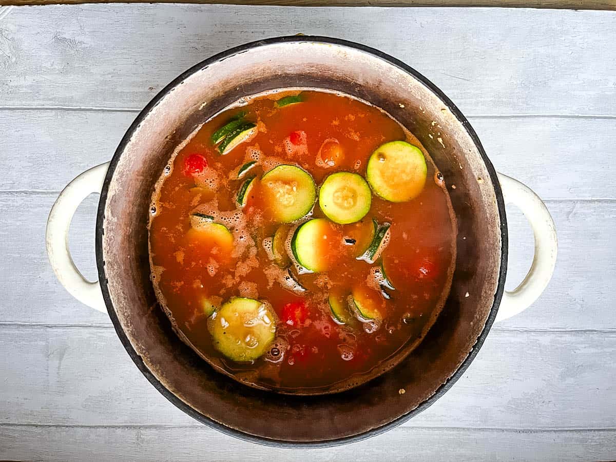 vegetable stock and tomato puree added to risotto rice and courgettes in pan.