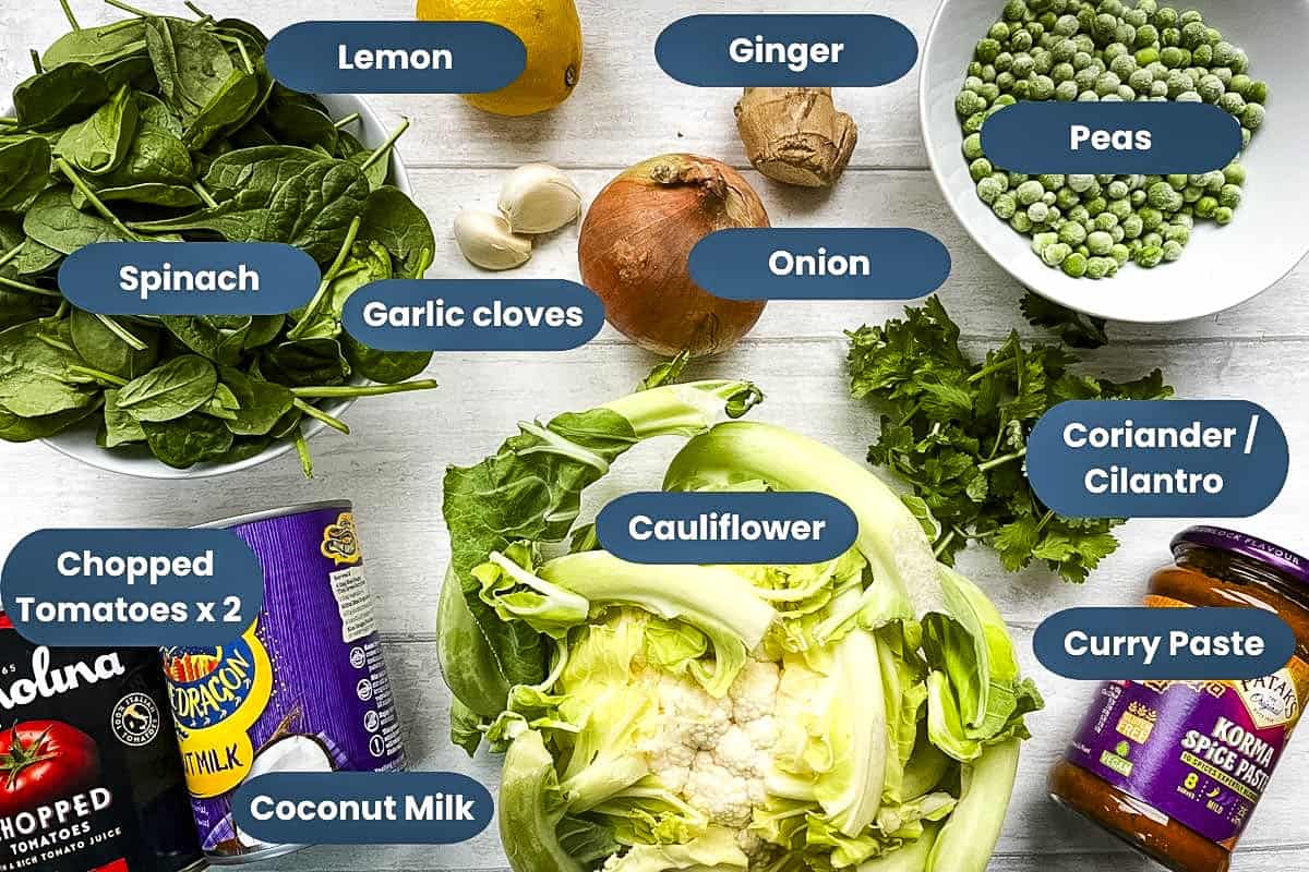 ingredients for cauliflower curry, spinach, lemon, ginger, peas, garlic cloves, onion, coriander, chopped tomatoes, coconut milk, cauliflower, curry paste.