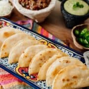 plate of crispy potato tacos with selection of sides in background.