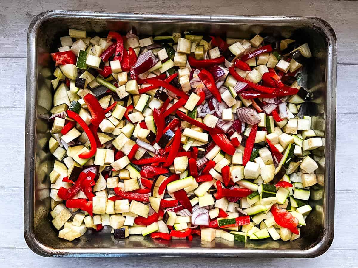 aubergine courgettes red onion and red pepper diced in roasting tray.