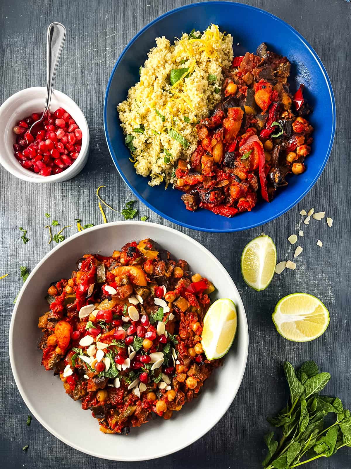 two bowls of aubergine tagine served with lemon couscous, pomegranite seeds and side of lime.