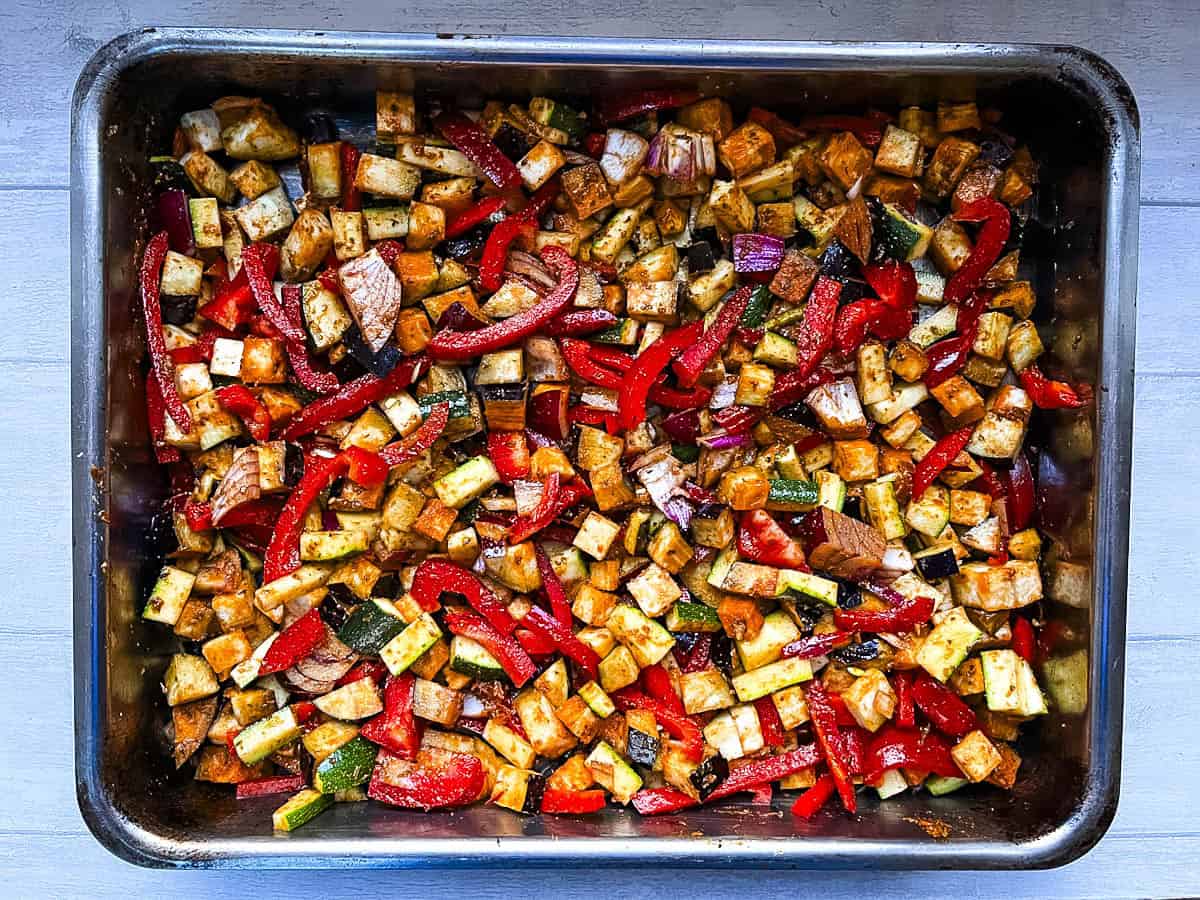 diced aubergine, courgette, red onion and red pepper coated in tagine spice ras-el-hanout in roasting tray.