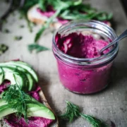 jar of beetroot hummus with some spread on bread topped with avocado and dill.