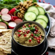 aubergine or eggplant dip topped with pomegranite seeds on a platter with fresh vegetables.