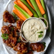 plate of vegan buffalo wings next to dip and chopped carrot and celery