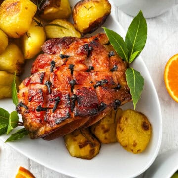 roasted gammon joint on plate with bay leaves and roasted potatoes