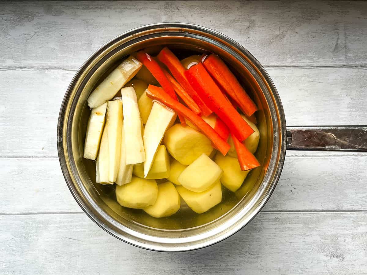potatoes carrot sticks and parsnip in pan ready for boiling.