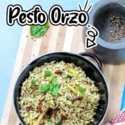 bowl of pesto orzo with sun dried tomatoes, summer squash and courgette topped with fresh basil leaves.