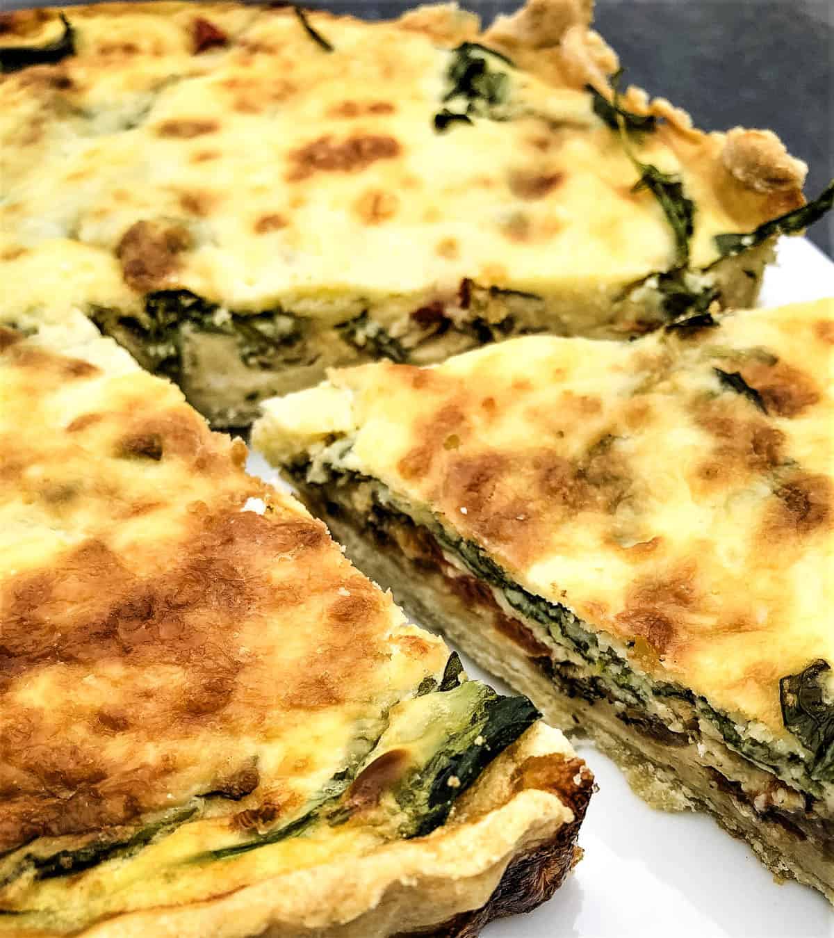 whole quiche cut with slice removed to see inside spinach filling.