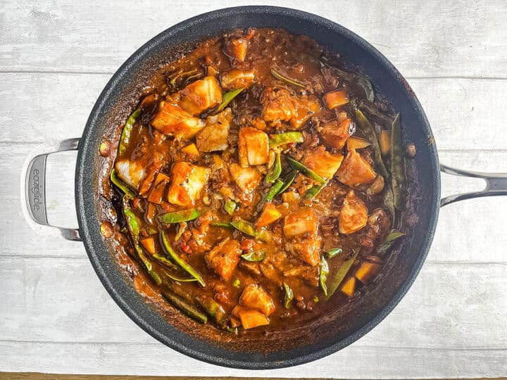 keralan fish curry with coconut milk and mango in pan.